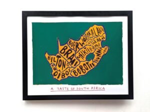Framed artwork of South Africa's map outlined in orange on green, filled with words like "Braai" and "Biltong." Text below reads "A Taste of South Africa."