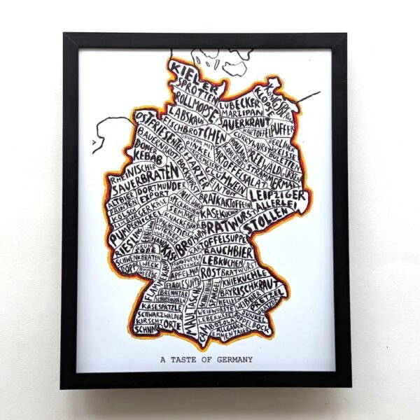 Framed artwork of Germany's map filled with handwritten German food names in bold black letters. Bright outline, labeled "A Taste of Germany."