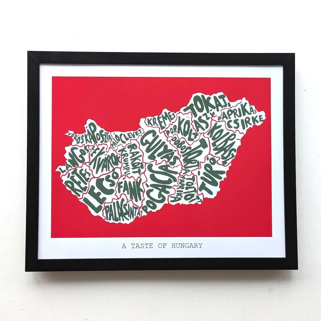 Framed artwork showing Hungary's map in text form with names of local dishes. The map is set against a bold red background. Text reads "A Taste of Hungary."