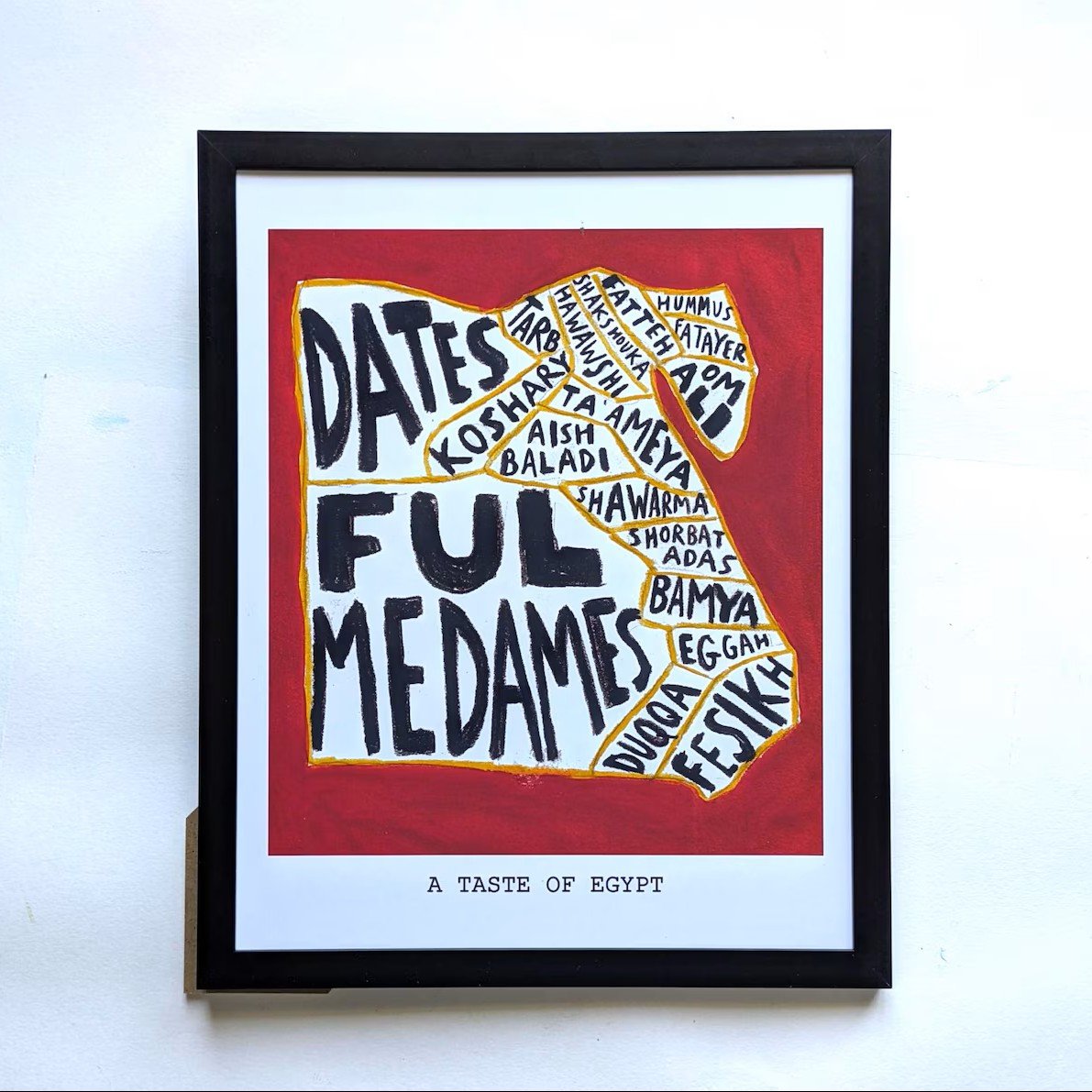 Framed art depicting Egyptian food names in bold black text on a red background, shaped like Egypt. Reads "A Taste of Egypt" below, conveying cultural richness.