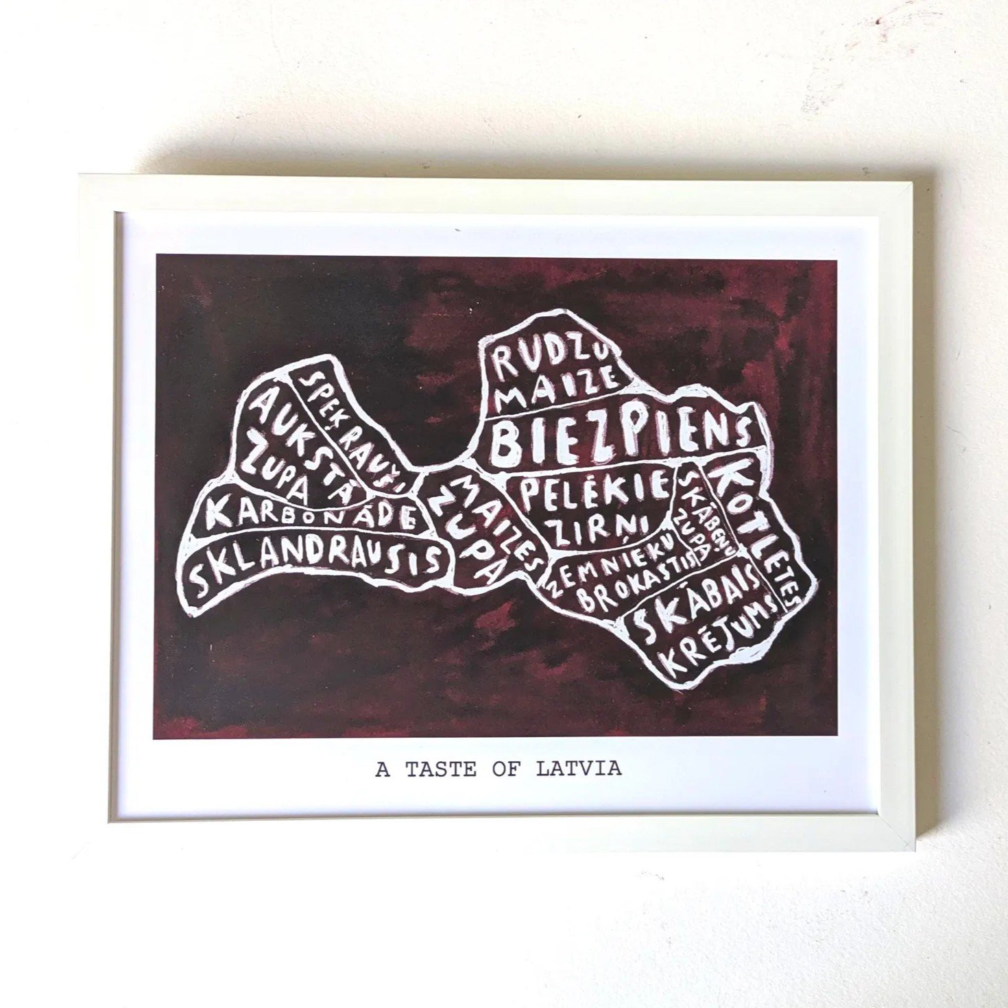 Map of Latvia filled with names of traditional foods like "Rudzu Maize" and "Biezpiens" in white text on a dark red background. Caption reads: "A Taste of Latvia."