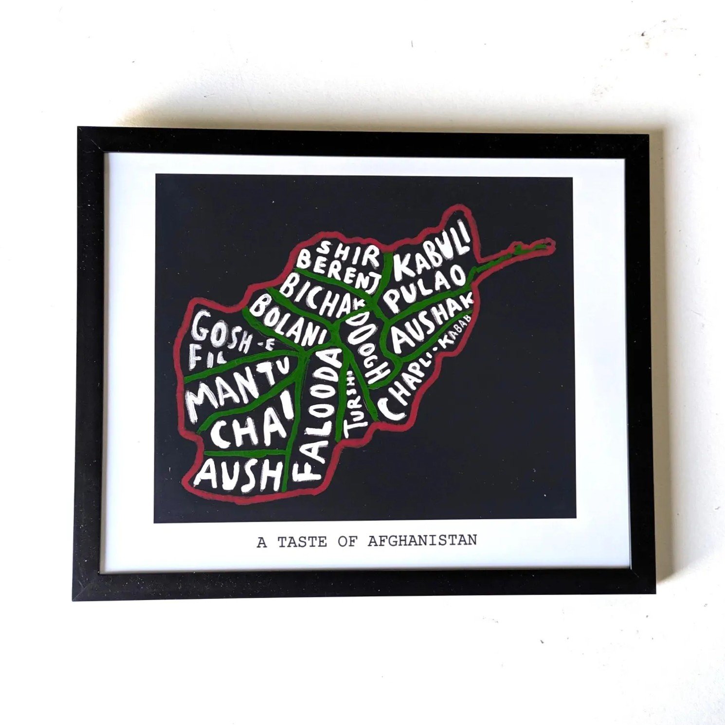 Framed artwork of Afghanistan's map filled with names of traditional dishes in white. Text below reads "A Taste of Afghanistan."