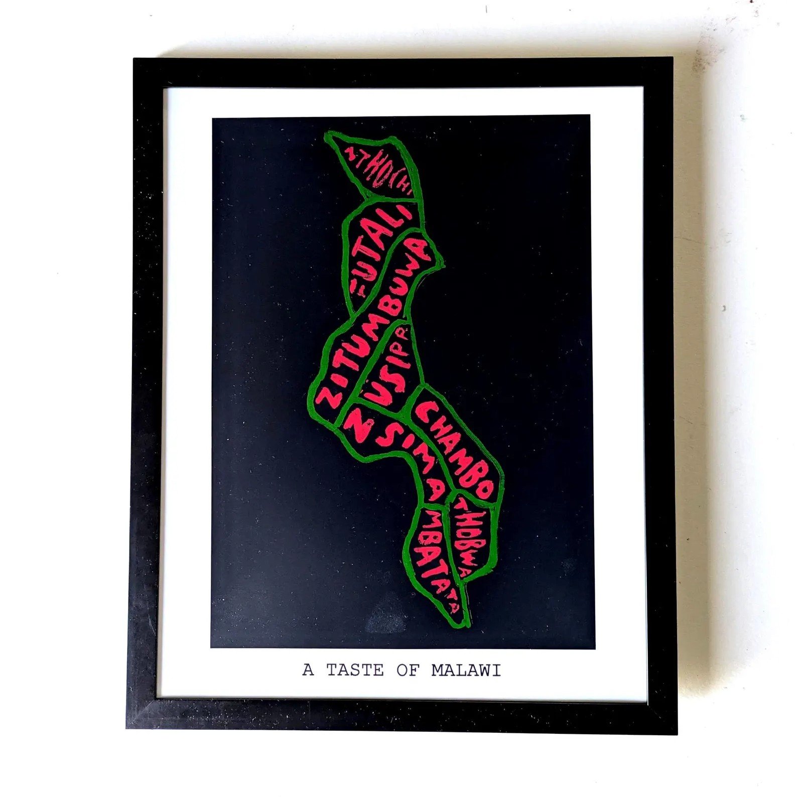 Map-shaped artwork of Malawi with words like "Nutali" and "Chambo" in red on black, outlined in green. Captioned "A Taste of Malawi."