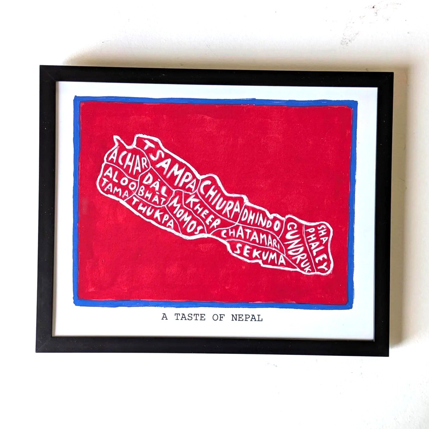 Framed artwork showing an outline of Nepal on a red background, filled with names of Nepali dishes like Momos and Kheer. Text below reads "A Taste of Nepal."