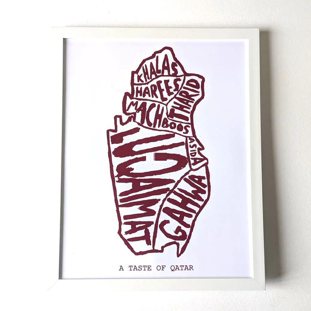 Framed artwork depicting Qatar’s shape filled with names of traditional dishes like machboos and luqaimat in bold maroon text. Caption reads "A Taste of Qatar."